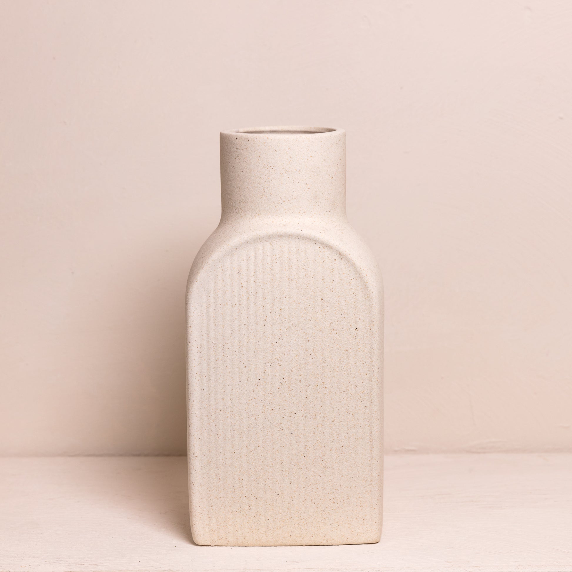 Minimalistische, rechthoekige vaas met afgeronde hoeken, uitgevoerd in een zachte zandkleur en voorzien van een subtiele ribbelstructuur.